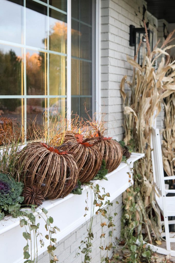 A picture of wicker pumpkins and flowering kale in a white window box.