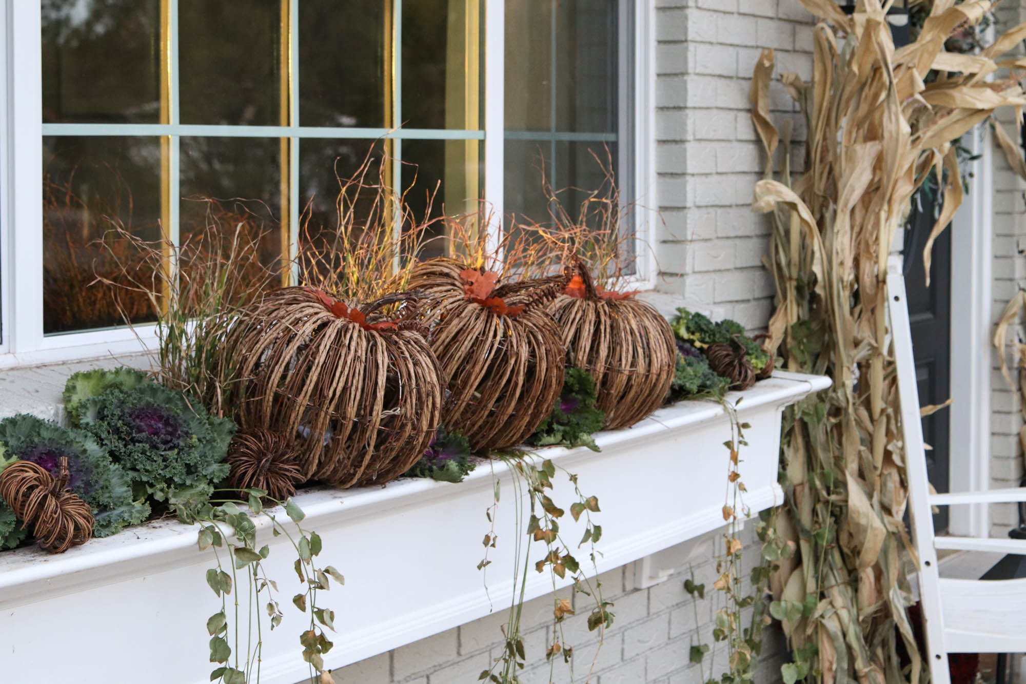 A picture of wicker pumpkins and flowering kale in a white window box.