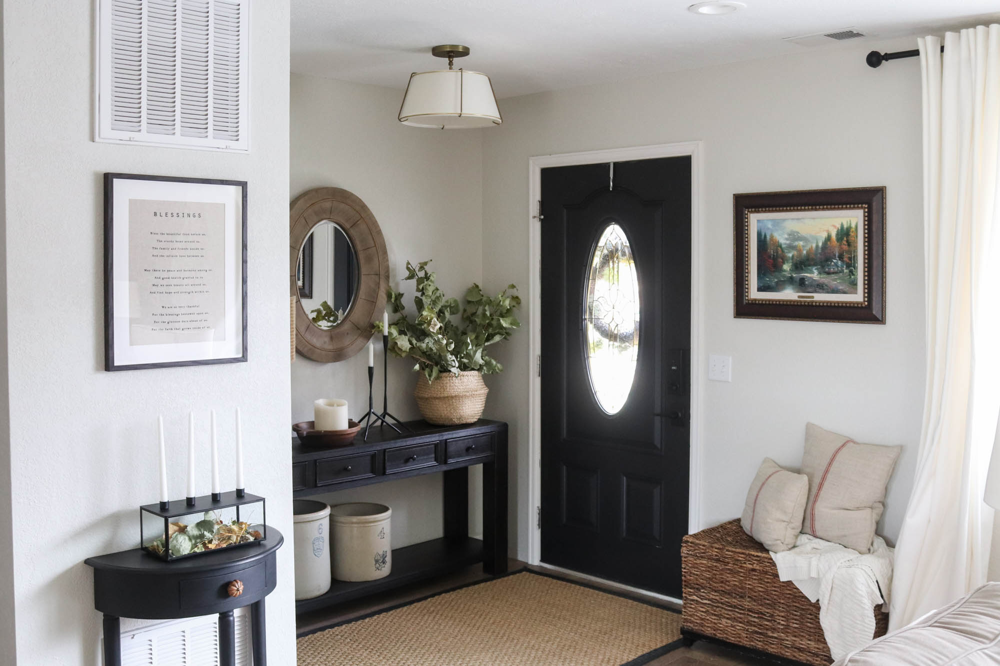 A picture of an entry with a hanging light fixture, side table and black front door.