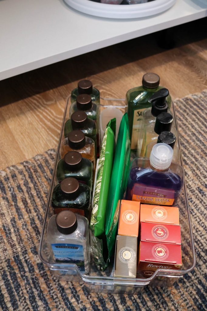 A picture showing the first step of organizing under the kitchen sink: organizing some bulk cleaning supplies in an acrylic tote. 