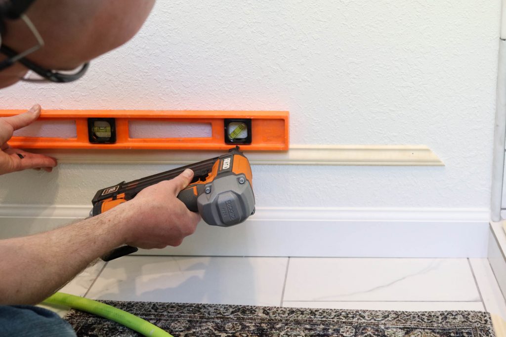 A picture of Todd nailing the moulding strip to the wall. 